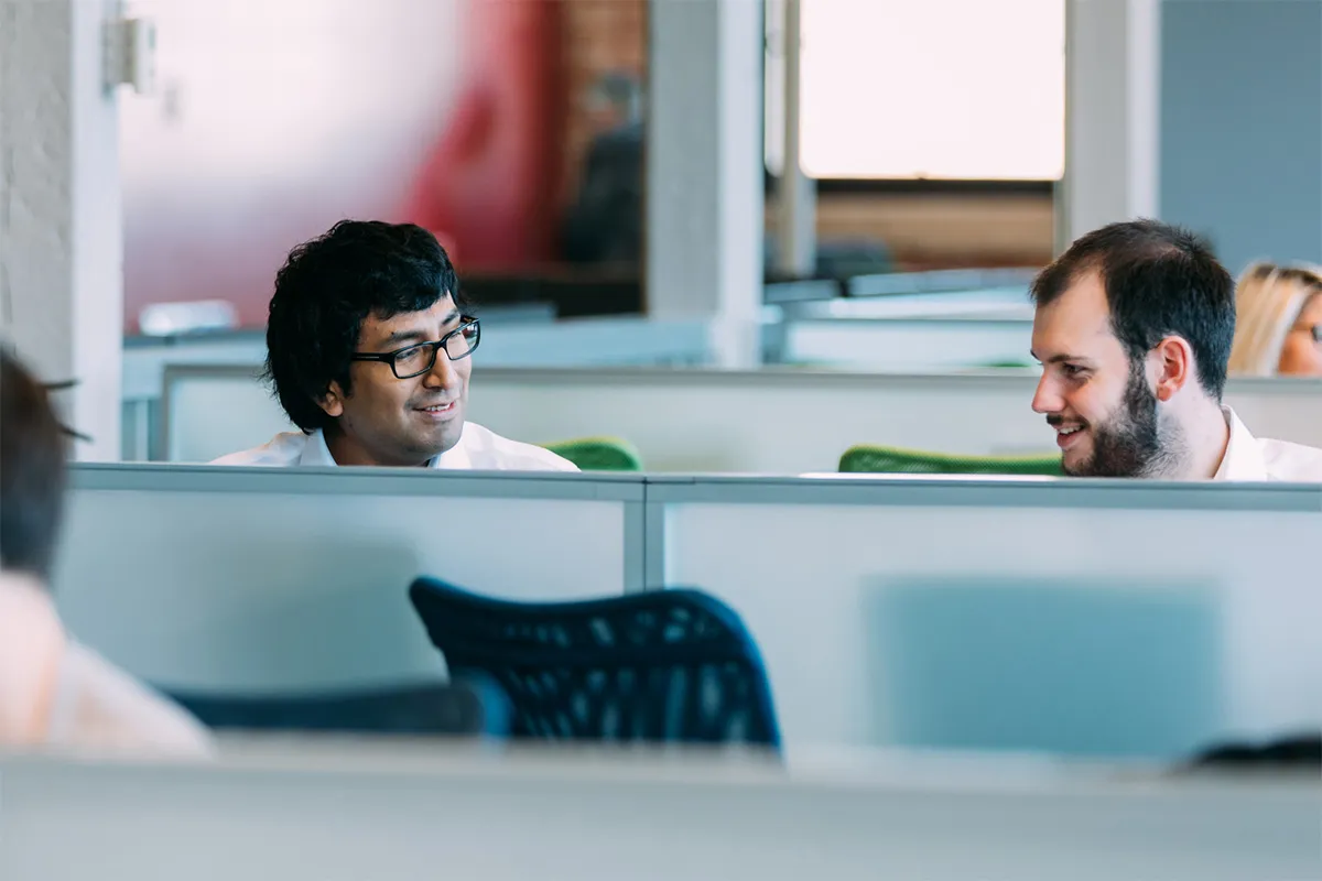 Two colleagues smiling and talking across office cubicles.